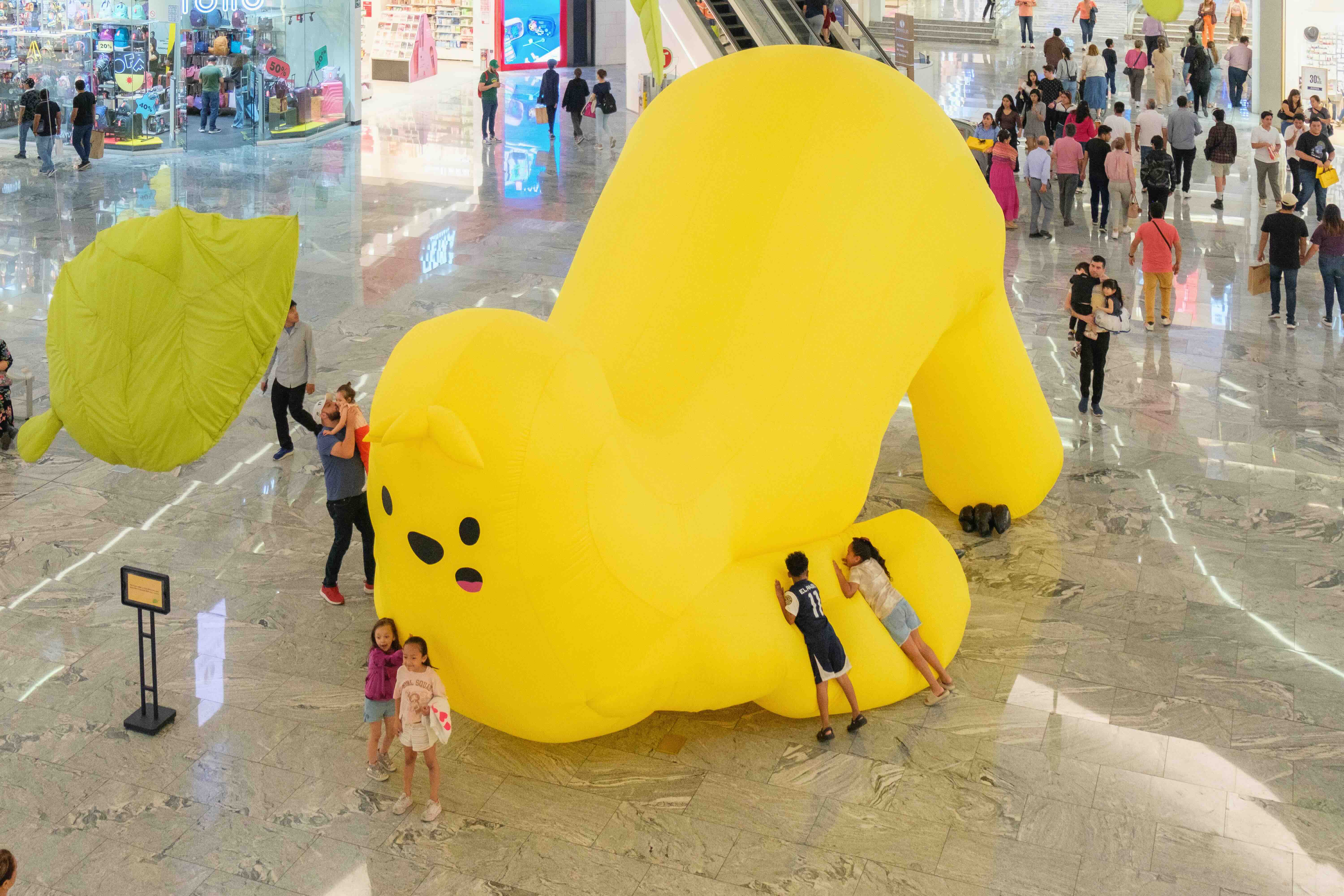 Children as Co-Creators of Urban Spaces: A Paradigm Shift in Latin America - MASSIVart - A giant inflatable yellow sloth in the middle of a mall in Mexico City. Children playing around it. 